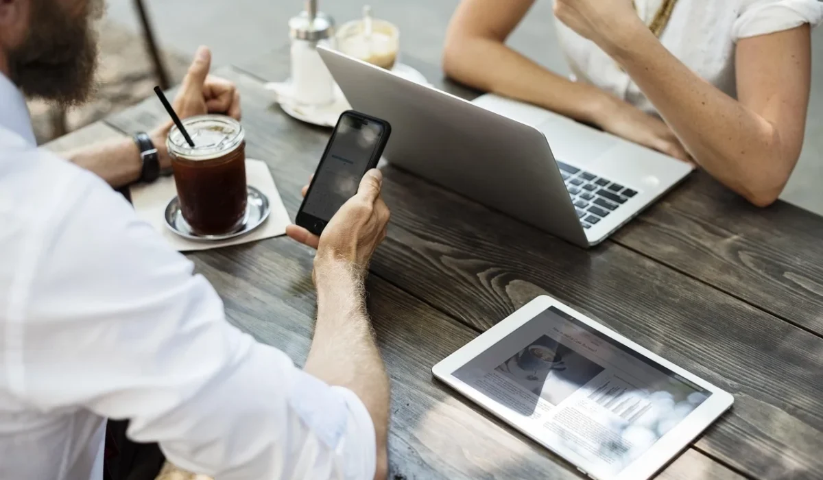 People collaborating with coffee, smartphone, laptop, and tablet at outdoor cafe table